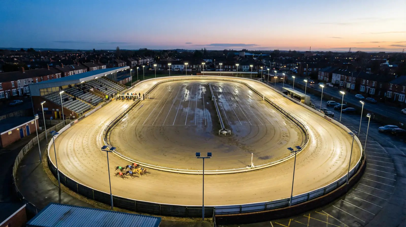 UK greyhound racing tracks — aerial view of a floodlit oval greyhound stadium at dusk