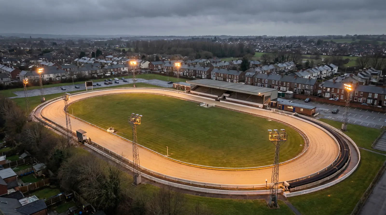 Aerial view of an oval greyhound racing stadium with sand track and floodlights in England